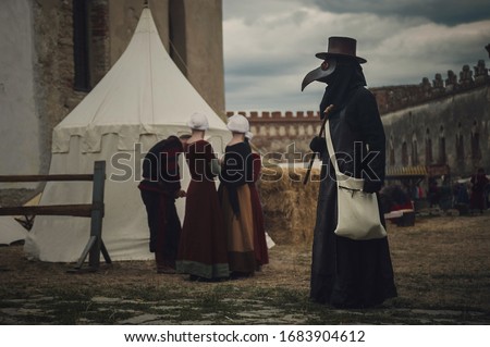 A masquerade historical scene reconstruction. Plague doctor in medieval old town. Castle and epidemic Royalty-Free Stock Photo #1683904612