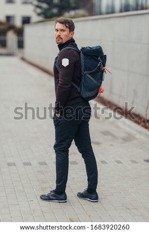 Handsome man in the urban environment. He has a backpack on his back. He goes on a journey.