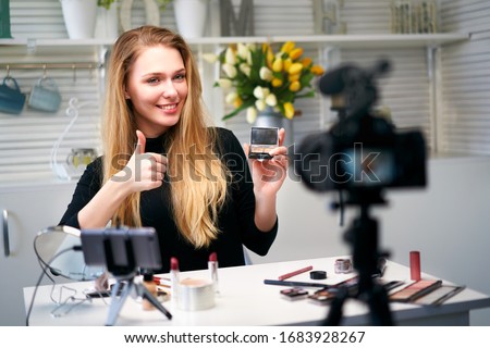 Beauty blogger woman filming daily make-up routine tutorial near camera. Influencer girl live streaming cosmetics product review. Vlogger female recommends eye shadow palette showing thump up sign. Royalty-Free Stock Photo #1683928267