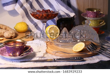 A vase of jam on a long leg, a cup of hot tea, lemon on a table on a towel
