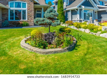 Flowers, nicely trimmed bushes and stones in front of the house, front yard. Landscape design.