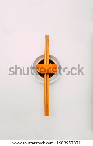 Stock photo of salmon nigiri sushi balanced on two chopsticks in a bowl of soy sauce. All on white background. Cenital plane.