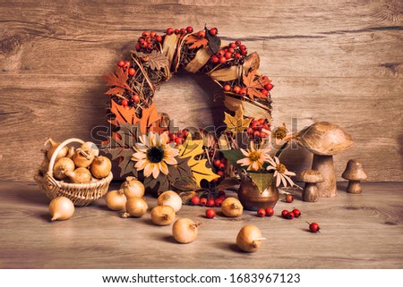 Autumn Thanksgiving arrangement with wreath decorated with orange berry felt Fall leaves and ribbons. Basket of onions, decorative pumpkins, Autumn leaves and flowers on aged wooden table, mushrooms.
