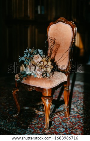 bride's wedding bouquet of white, yellow, pink roses with eucalyptus stands on a stylish chair in a dark room