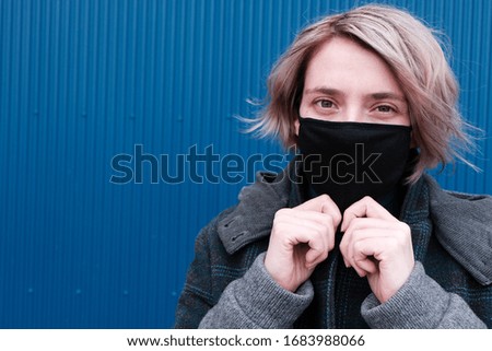 Young woman on a city street in a protective mask for the spread of the flu virus and disease. Girl with a black mask on her face, protected from bacteria on the street