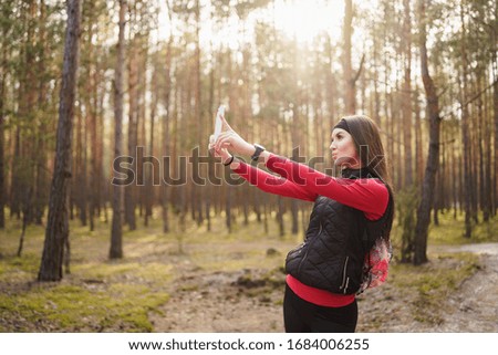 Caucasian girl is hiking at the weekend in a pine forest green and lush beautiful. She is taking some photo. She has a beautiful smile. Healthy lifestyle concept. 