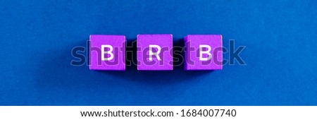 Top view image of BRB abbreviation spelled on violet colored wooden dices. Over  blue background.
