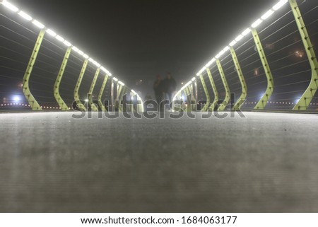 blur image of people walking across illuminated footbridge, Docklands, London 