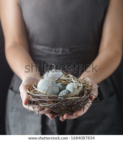 Woman hands holding nest with marble Easter eggs with feathers on dark background with light. Happy Easter holiday, selective focus