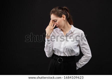 Girl in a white shirt rubs forehead from fatigue on a black background. Close up.