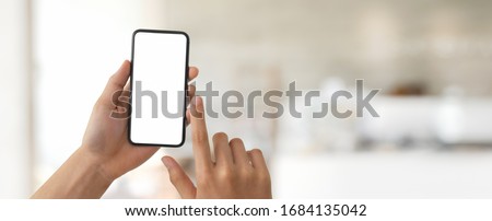 Cropped shot of a man touching on blank screen smartphone in blurred glass partition office room background