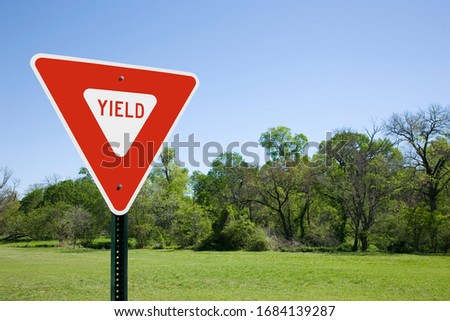 Red Yield Sign With Blue Sky, Green Trees and Grass