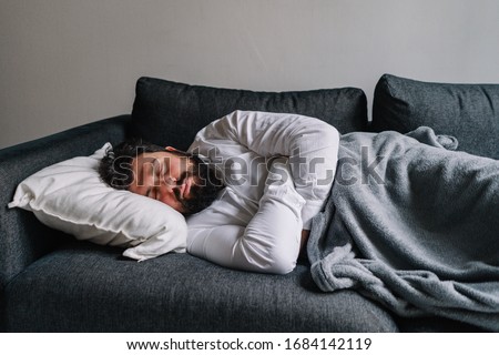 Young elegant man sleeping on a sofa, tired guy feeling exhausted after work and sleeping during daytime, a nap at home on the couch
