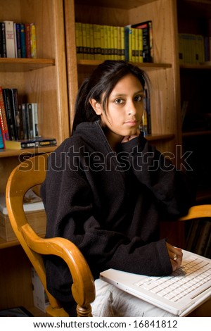 Young Hispanic teenager using a laptop in the library. Looking at the camera. Serious