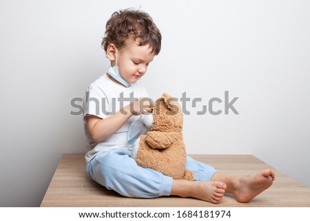 child, a boy in a medical mask puts on a mask on a teddy bear. Teaching a child to protect and prevent quarantine from cornavirus. Royalty-Free Stock Photo #1684181974