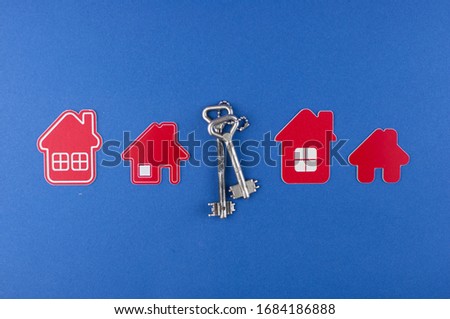 Key and house shaped keychain arrangement on blue background. Top view, flat lay. Real estate, insurance concept, mortgage, buy sell house, realtor concept 