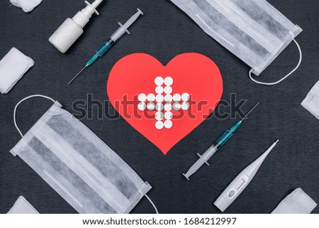 Some heart shape with medicine icon inside formed by pills with needles, thermometer, nose spray and masks on dark background, top view.