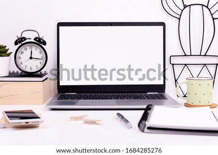 Laptop with blank monitor with mock up on office desk with coffee, book, clock, smartphone and pen. Home office with white office table. Copy space.