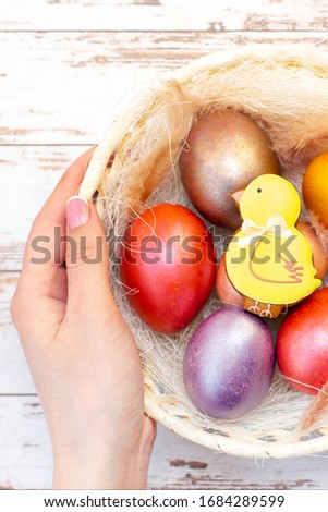 Easter holiday. Colored eggs in a basket. Easter gingerbread chicken in the basket, which is in the hands. on a light wooden background.  vertical photo