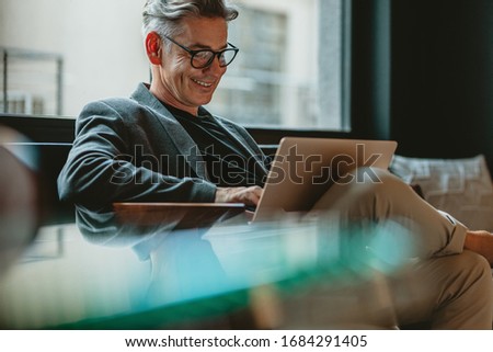 Smiling businessman sitting in office lobby working on laptop. Male business professional working in office lobby. Royalty-Free Stock Photo #1684291405