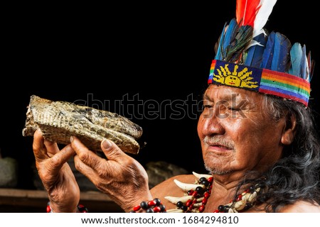 A shaman in the Amazon rainforest of Ecuador performs a sacred ayahuasca ritual, surrounded by feathers, snakes, and indigenous tribe members.