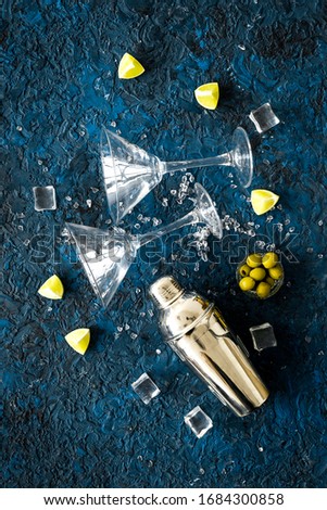 Bar background with martini glasses, shaker, ice, lemon and olives on blue table top-down