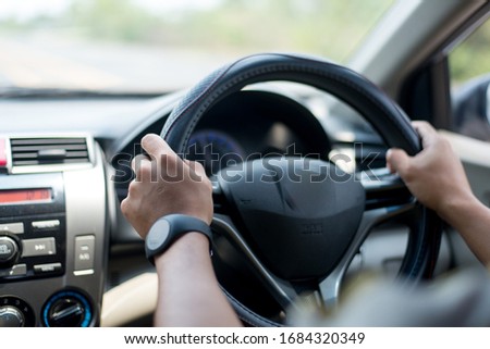 A young Asian man drives a car on a daytime road.