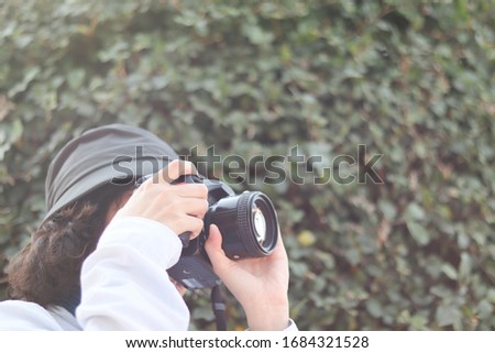 Soft focus hand of girl or photographer is taking a photo in travel and tourist / girl with gray hat and camera with blurred green leafs for copy space and background texture concept