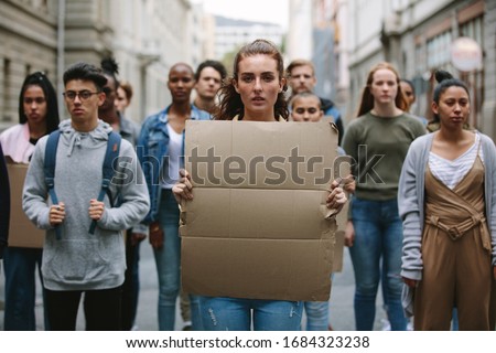 Woman activist in a strike with a blank banner protesting on the street. People doing demonstration on the street holding sign boards. Royalty-Free Stock Photo #1684323238