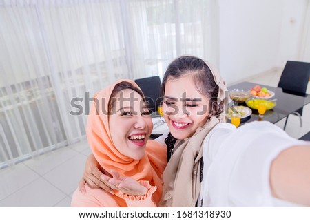 Beautiful muslim women taking selfie photo with a mobile phone in dining room at home