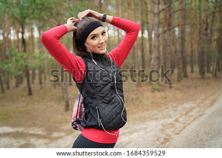 Young woman is walking in a pine forest at the weekend. She is listening 
favorite music. She has a beautiful smile. Healthy lifestyle and relax concept.