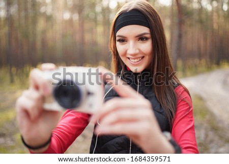 Young woman is walking in a pine forest at the weekend. She is taking some photo. She has a beautiful smile. Healthy lifestyle concept. 