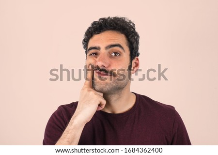 Portrait of a young boy with a mustache forcing a smile, holding his fingers at the edges of his lips. Purple t-shirt and isolated white background.