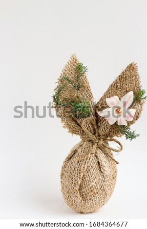 Chicken egg decorated with burlap like an Easter bunny rabbit and with flowers on white background. Minimal creative concept, card, illustration of Easter, gift, present. 