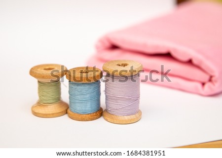 Set of tailoring accessories. Close up of a stack of folded pink fabric, sewing scissors, and spools of thread