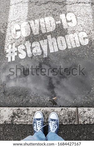 Feet of a man in sneakers shoes standing on gray sidewalk with hashtag #stayhome (COVID-19). Coronavirus in the world. COVID-19 alert banner. 