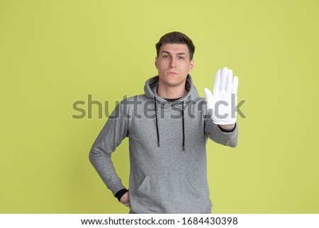 Showing stop sign. Caucasian man's portrait isolated on yellow studio background. Freaky male model using gloves. Concept of human emotions, facial expression, sales, ad. Unusual appearance.
