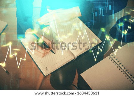 Forex chart hologram on hand taking notes background. Concept of analysis. Multi exposure