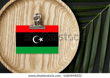 Libya flag tagged on wooden plate. Tropical palm leaves monstera on background. Minimal national concept.