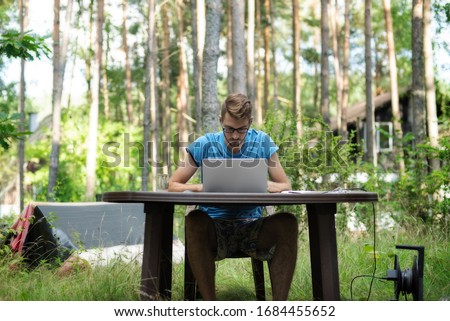 A man working remotely on his laptop on a table outdoor among the trees. It looks like he works in a jungle Royalty-Free Stock Photo #1684455652
