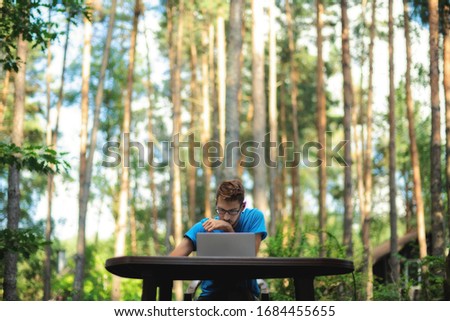A man working remotely on his laptop on a table outdoor among the trees. It looks like he works in a jungle Royalty-Free Stock Photo #1684455655