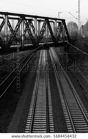 Parallel Railway Tracks near Schwerte Ruhr Germany with steel construction bridge crossing, black and white greyscale with concrete thresholds and overhead lines. Main line connecting Hagen with Hamm.