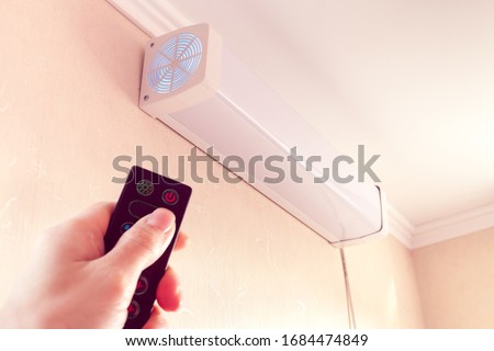 hand from remote-controlled includes bactericidal air recirculator hanging on wall for quartzing air in room Royalty-Free Stock Photo #1684474849
