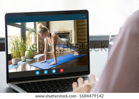 Focus on computer screen with fit young woman standing in plank position, enjoying practicing yoga on mat alone at home. Strong female fitness trainer giving online educational pilates workshop. Royalty-Free Stock Photo #1684479142