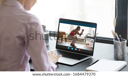 Back rear view young woman sitting at home office workplace, watching educational fitness training video on laptop. Screen view healthy trainer in sportwear doing squats, presenting online course. Royalty-Free Stock Photo #1684479370