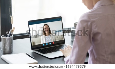 Rear back shoulder view young woman sitting at office table, communicating with smiling sister via video call. Happy female friends talking speaking chatting, using computer videoconference app. Royalty-Free Stock Photo #1684479379
