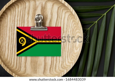 Vanuatu flag tagged on wooden plate. Tropical palm leaves monstera on background. Minimal national concept.