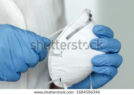 Hands with blue protective nitride gloves holding  N95, FFP2 respirator, face mask. Coronavirus, COVID-19 concept. Selective focus. Royalty-Free Stock Photo #1684506346