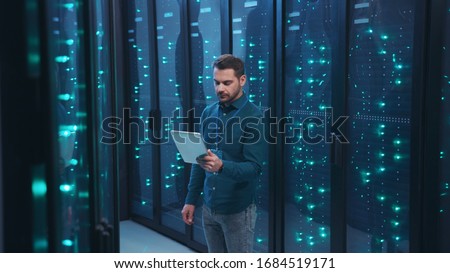 IT professional with digital tablet monitoring system performance of database network servers working on rack in high tech data center. Webhosting, cloud computing. Royalty-Free Stock Photo #1684519171