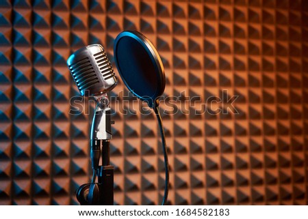 Retro microphone and pop filter for singing or recording a podcast on acoustic foam panel background, colorful light